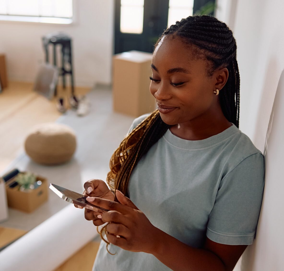 Woman standing in a new home checking information on her phone, with moving boxes in the background.