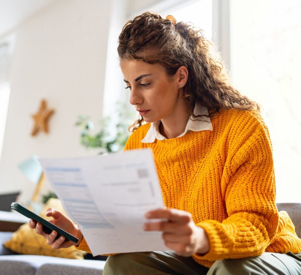 Homebuyer reviewing financial documents and checking expenses on a phone at home.